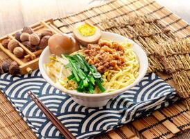 Dry noodles with minced pork meat and preserved egg with chopsticks served in dish isolated on napkin side view on table taiwan food photo