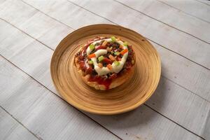 mini chicken pizza topping with tomato, cucumber, mayo and chilli sauce served in dish isolated on napkin bangladeshi food side view on table photo