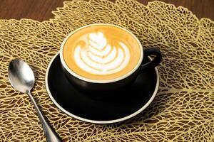 cappuccino with art and spoon served in coffee cup isolated on wooden table side view of cafe hot drink photo