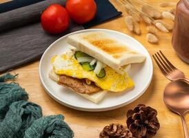 Pork Chop and Egg Toast with cherry tomato, spoon and fork served in dish isolated on wooden table side view of taiwan food photo