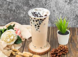 iced Pearl milk tea with ice cube served in disposable glass isolated n table side view of taiwanese drink photo