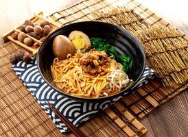 sesame paste noodles with minced pork meat, preserved egg and chopsticks served in plate isolated on napkin side view on table taiwan food photo