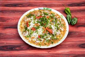 Spicy Naga Chotpoti with green pepper include chickpea, tomato, onion, cabbage, chilli, coriander, and sauce served in plate isolated on wooden table side view of bangladeshi street food photo