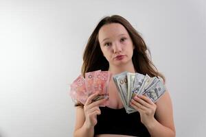 choice between Canadian dollars and US dollars girl weighs in her hands a pack of five banknotes of Canadian dollars with large pack of 100 dollar bills twisting lips chooses a lot of money trip gift photo