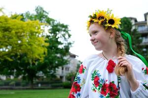 beautiful red-haired Ukrainian girl in an embroidered blouse flowers red poppies on a white shirt sunflowers wreath in hair ribbons nature Ukraine patriotism national clothing is coming into fashion photo