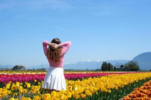 colección de videos y fotos dónde un niña en un blanco falda camina mediante campo con tulipanes azul antecedentes cielo montañas brillante floración campos adolescente joven mujer caminar al aire libre belleza cuidados personales