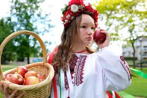 young beautiful girl in red wreath of flowers on her head red poppies in vyshyvanka red apples take an apple with hands inhale smell good weather in garden For world beautiful girls women of the world photo