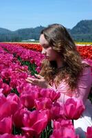 a young girl teenager stands in beautiful bright pink Corolla tulips inhale the fragrance of flowers straighten her hair look into the distance beautiful field in spring unusually bright color photo