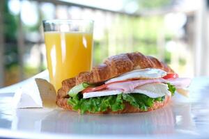 cuerno con balyk y Pepino lechuga hojas tomate delicioso desayuno con queso y naranja jugo blanco plato tocino capas en emparedado en el balcón en negro mesa delicioso comida almuerzo bocadillo foto