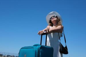 young girl in white dress and huge hat with a suitcase travels around globe Close up woman legs walks on asphalt road and traveling world with travel suitcase . Female hitchhiking around country photo