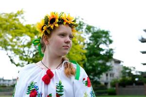 beautiful red-haired Ukrainian girl in an embroidered blouse flowers red poppies on a white shirt sunflowers wreath in hair ribbons nature Ukraine patriotism national clothing is coming into fashion photo