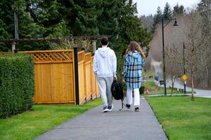 adolescente chico y niña espalda a colegio en el privado sector, dos personas desde colegio son caminando a lo largo el acera con un mochila en su manos con su espaldas a el cámara privado sector foto