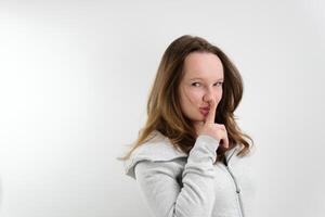 a young teenage girl puts her finger to her lips secrecy don't tell anyone sharply turn around look into the frame wave a finger negatively on a white background stern look photo