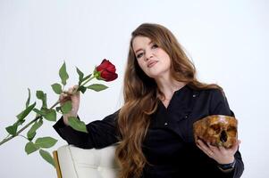 insidious cruel woman vamp strong serious woman in her hands with a rose and a human skull sits on a white background in black clothes medicine power love Lost opportunities Life and death photo