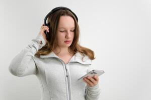 girl with her finger taps on professional headphones listen to music check quality in hands holds white smartphone mobile phone internet wi-fi on white background laughs smile makes eyes photo