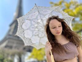 a girl with a white parasol stands against the backdrop of the Eiffel Tower with her back to us can be used for advertising for the Internet for travel agencies photo