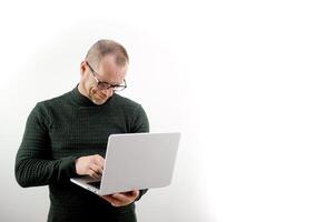 Focused man in glasses using a laptop, typing on the keyboard, writing an email or message, chatting, shopping, a successful freelancer working online on a computer space for text ad social networks photo