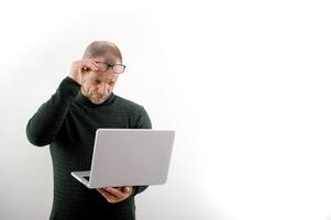 adult man with laptop wearing glasses looks at screen vision has fallen age-related problem is bad seeing put glasses on nose eye treatment vision correction white background ad space text see light photo