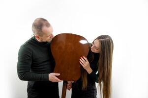 man and woman fooling around with a guitar turned it upside down talking leaning their chin on a white background a couple in love having fun doing a photo shoot laughing posing