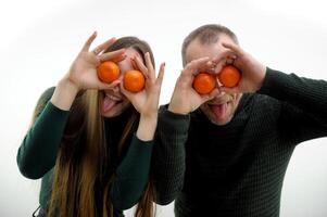 man and a woman are joking playing having fun they put a tangerine to their eyes laughing showing tongues on a white background green sweaters are the same fun the joy of making faces grimacing photo