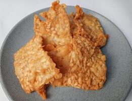 Delicious fried tempeh from Indonesia Asian culinary on the plate isolated on white background. Tempe goreng photo