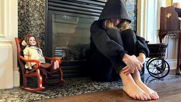 offended teenager teenager girl sitting by the fireplace with her legs bent and her head bowed she pulled the hood over her face she has a black sweatshirt and black jeans problems of adolescence photo