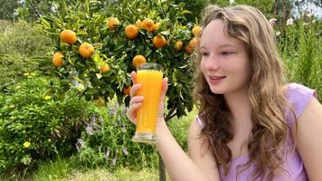 the girl drinks orange juice against the background of a tangerine tree, it can be orange juice tangerine mango she drinks greedily and really likes the juice delicious everywhere greens and summer photo