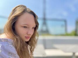 tender face of a girl with freckles close-up she has blond hair and bright eyes She looks and can be used for any advertisem ent there is a place for text Eiffel Tower in the background photo