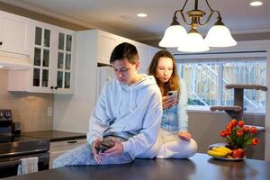 teenagers spend time on phones a boy and a girl 13-16 years old sit in the kitchen on the table everyone is busy with their gadget first date no time to sit on social networks on Internet to kill time photo