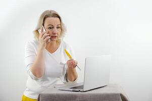 serious dissatisfied woman talking on the phone looks into a laptop in her hands scissors and a meter weight loss diet tired of communicating with a doctor nutritionist middle age white background photo