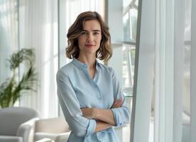 A smiling businesswoman stands in an office, arms crossed. photo