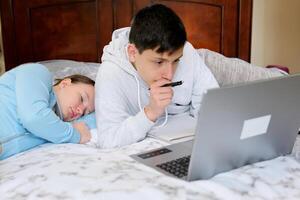 teenagers sit at computers do their homework online study and are not tired of studying go to bed fall asleep One works the other sleeps no desire to study eyes hurt need to rest photo