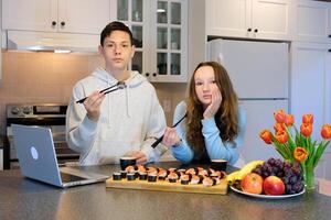 having fun teenage boy and girl watching movie on laptops eating sushi in kitchen food delivery fast food fun pastime pleasant relationship first date friends classmates together brother and sister photo