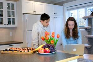 look at laptop lean over focused think look teenagers doing homework in the kitchen ordered sushi meet after school first date watch movie spend time together boy girl 13 14 15 years old photo