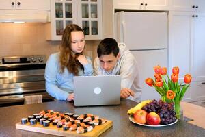 a girl brought a gift to her boyfriend for helping her online tutor work in the kitchen on a laptop then eat teenagers communicate spend time together help each other in their studies photo