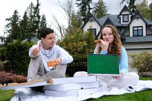 croma llave ordenador portátil con verde pantalla picnic en verde césped abierto caja con tejido de punto aguja agradable emociones divertido pasatiempo adolescentes primero fecha sentar pulgar arriba saboreo Pizza delicioso comida sorpresa alegría foto