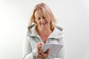 making plans for the future writing in a notebook with a pen, woman on a white background writes down ideas plans for the day of purchase, decisions to think, raise her head, look into the frame photo