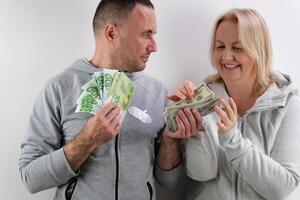 surprise on the face Men have a lot of money in their hands bake their lower lip woman wants more than 100 dollar bills husband wife emotions middle age man and woman with money on white background photo