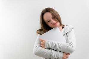 Win Concept. Portrait of smiling asian lady hugging notebook with black empty screen, holding it tight near chest. Positive female nerd posing isolated over pastel studio background wall, copy space photo