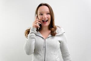 imagen de hermosa sonriente rubia mujer hablando en Teléfono móvil y reír, teniendo negocio llamada en móvil teléfono, en pie en rojo chaqueta de sport en contra gris antecedentes. negocio y tecnología foto