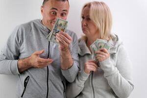 surprise on the face Men have a lot of money in their hands bake their lower lip woman wants more than 100 dollar bills husband wife emotions middle age man and woman with money on white background photo