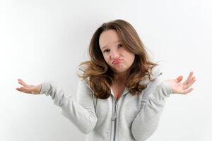 Puzzled young caucasian woman looks uncertain and confused, shrug shoulders in hesitation, spreading hands in obscurity over white background for your advertisment or promotional text photo