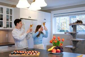 Happy interracial couple dancing in the kitchen, singing while cooking breakfast or dinner, young American woman and a handsome man smiling and having fun together, holding kitchen utensils photo