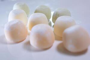 different flavors of Asian dessert mochi, a woman hand takes out sweet ice cream made from peas and rice starch dough from a box onto a white plate photo