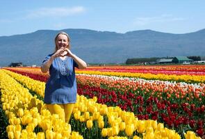 adulto mujer en campo de tulipanes ropa azul amarillo me gusta bandera de Ucrania alegría felicidad en montañas floreciente amarillo flores libertad frescura aire amarillo pantalones azul blusa rubio ordinario hembra foto