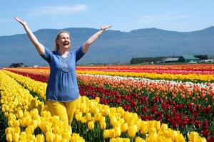 adult woman in field of tulips clothes blue yellow like flag of Ukraine joy happiness in mountains blooming Yellow flowers Freedom freshness air yellow pants blue blouse fair-haired ordinary female photo