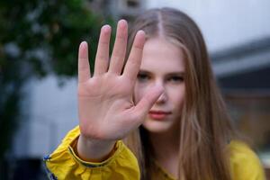 beautiful young woman in yellow shirt shows palm forward invasion violence against racial gender discrimination. Determined European woman makes a protest sign against domestic violence or abortion. photo