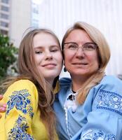 madre y hija en bordado camisas azul y amarillo blusa linda familia relación de cerca retrato cara al aire libre contento mayor mujer disfrutando en hija afecto en de la madre día. foto