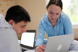 un chico ayuda un niña a hacer deberes en un ordenador portátil blanco pantalla espacio para publicidad texto dos adolescentes estudiar en línea en un habitación sentar enfocado trabajo estudiar ligero ropa blanco personas europeo americanos foto