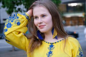 el niña es vistiendo un bordado camisa, nacional ucranio ropa eslava, un amarillo camisa. enderezar pelo con manos largo colgado pendientes en azul y amarillo bordado azul flores foto